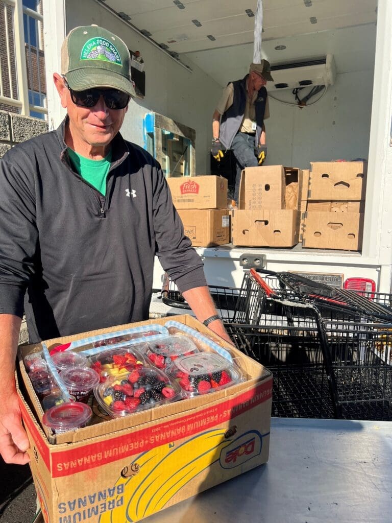 GR-Safeway-Strawberries - Helena Food Share Two men unload boxes of fruit from a service truck; berry cups visible in the foreground act as the product being moved.