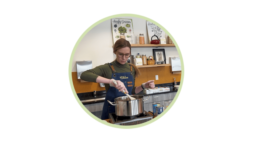 Woman wearing a blue apron labeled Chloe stirs a pot on a stove in a kitchen.