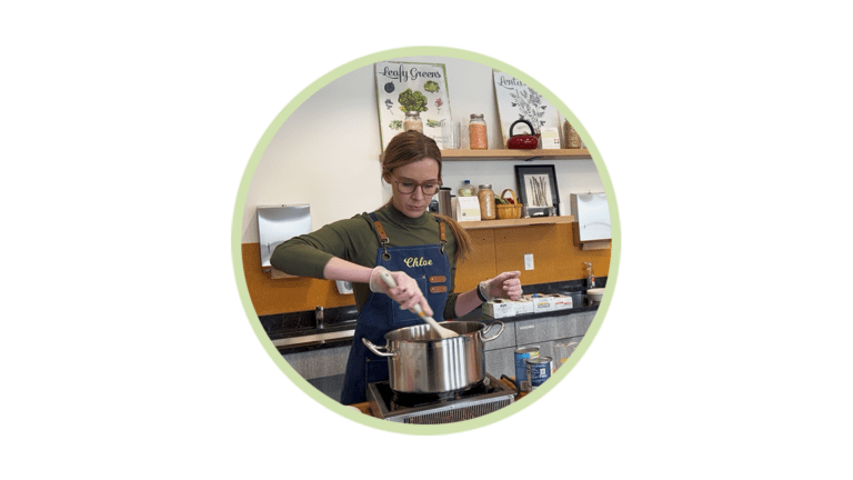 Woman wearing a blue apron labeled Chloe stirs a pot on a stove in a kitchen.