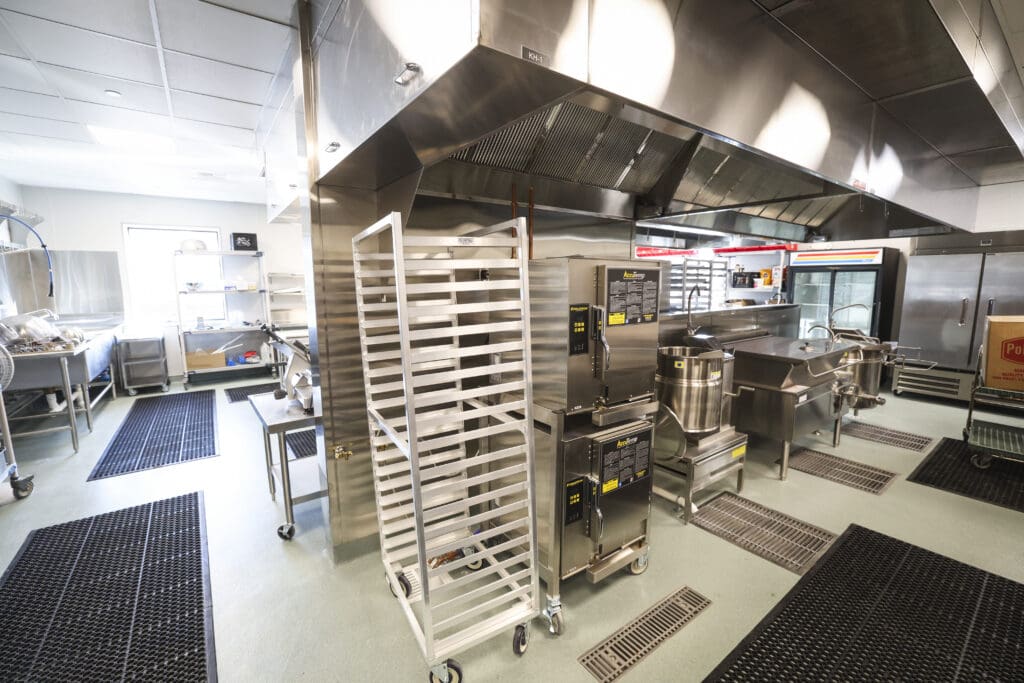 Industrial stainless steel kitchen with large exhaust hoods and racks in a busy prep area