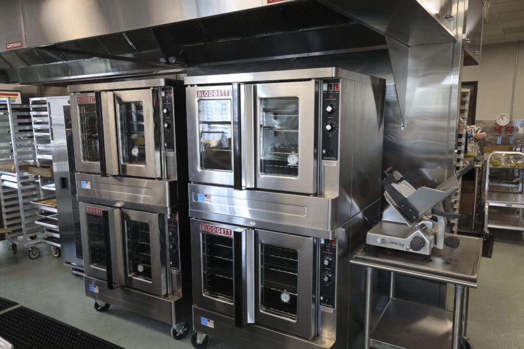 Row of Blodgett stainless steel ovens in a commercial kitchen with a large vent hood above.