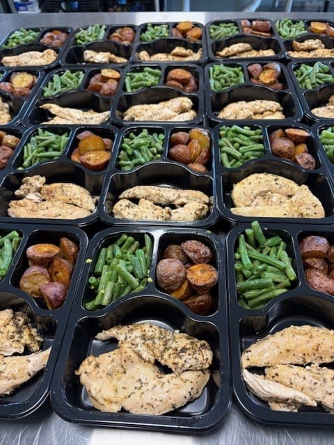 Meal-prep containers with seasoned chicken, green beans, and roasted potatoes in each compartment