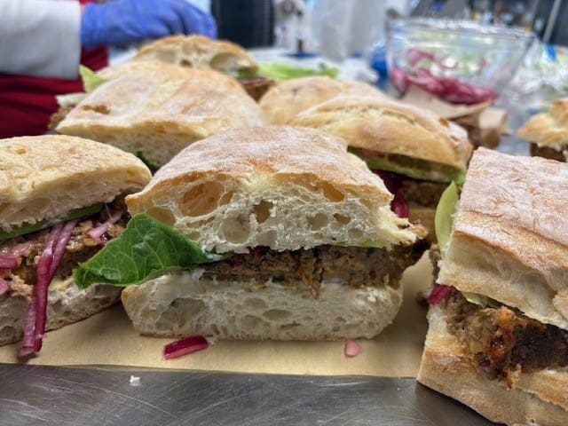 Close-up of crusty baguette sandwiches filled with spiced ground meat, lettuce, and red onions on a parchment-lined surface.