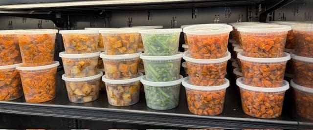 Clear plastic containers filled with assorted diced vegetables, stacked on a supermarket shelf by the dozen.